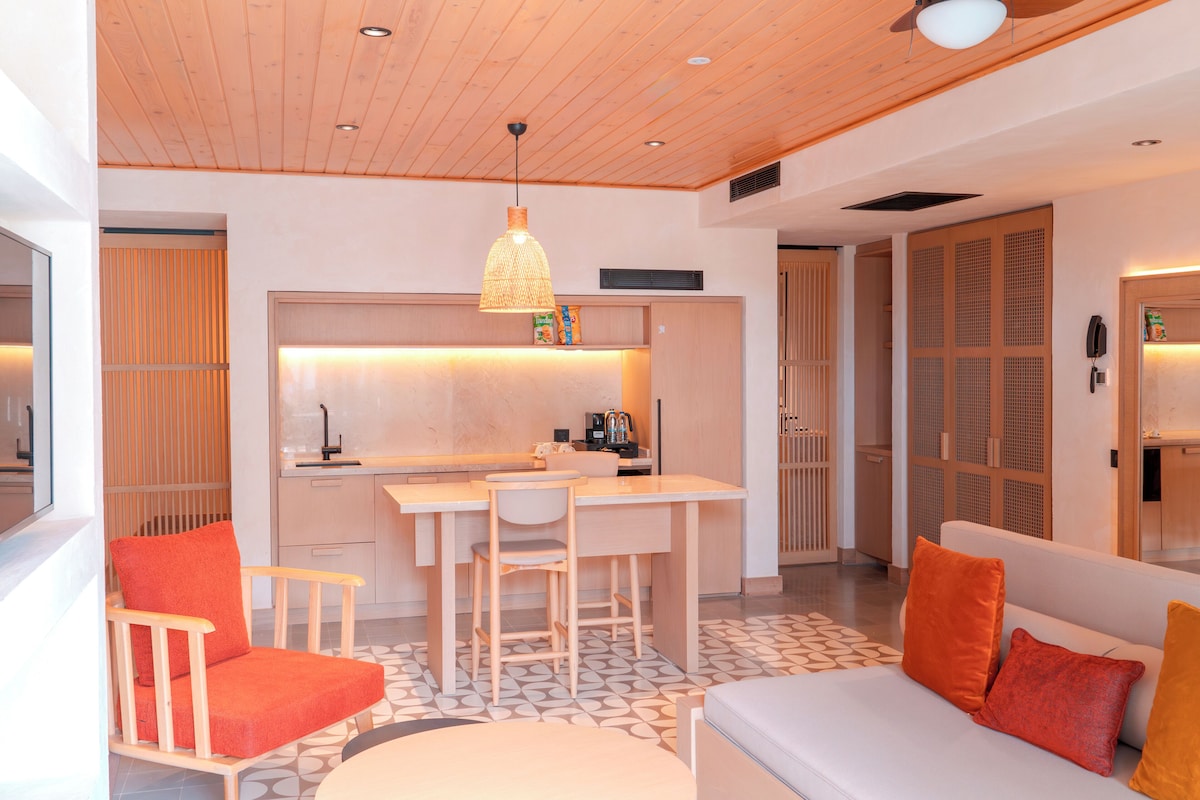 Una cocina moderna con zona de comedor, techo de madera y un sofá con cojines naranja.