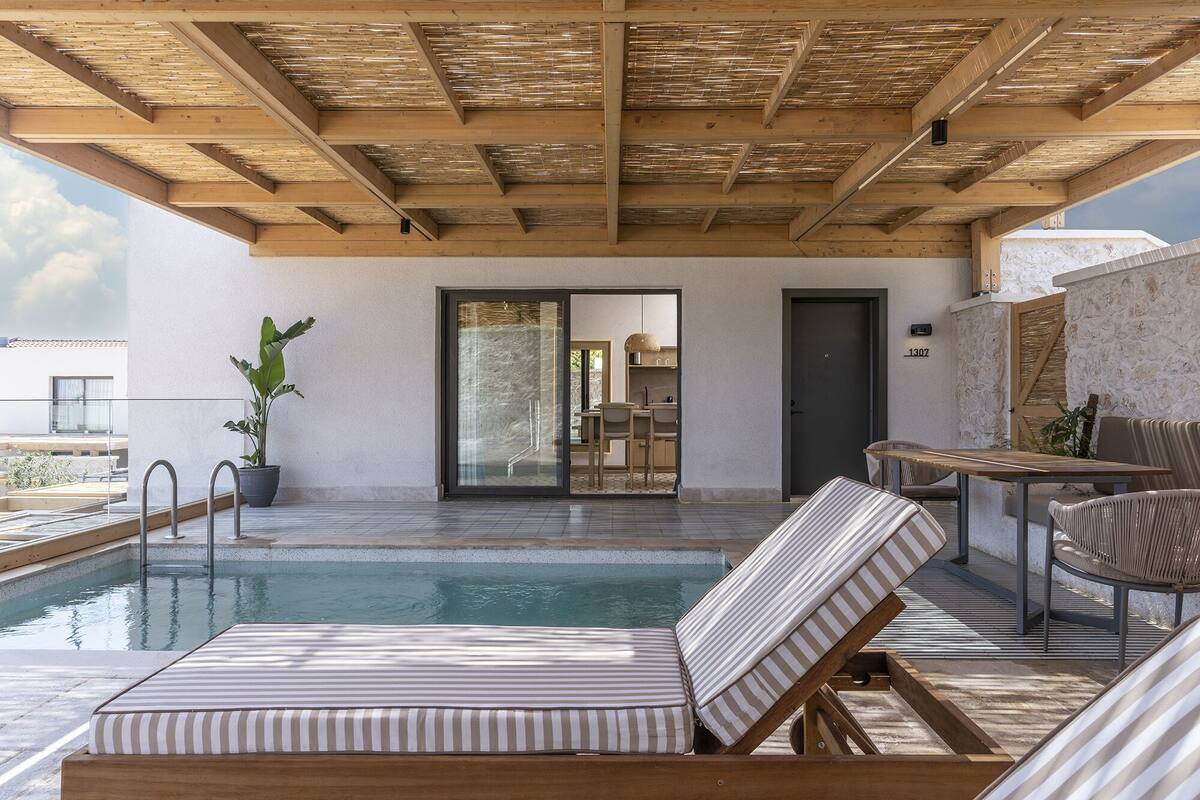 Un área de piscina con sillones de descanso, una mesa y una puerta que da a una cocina.