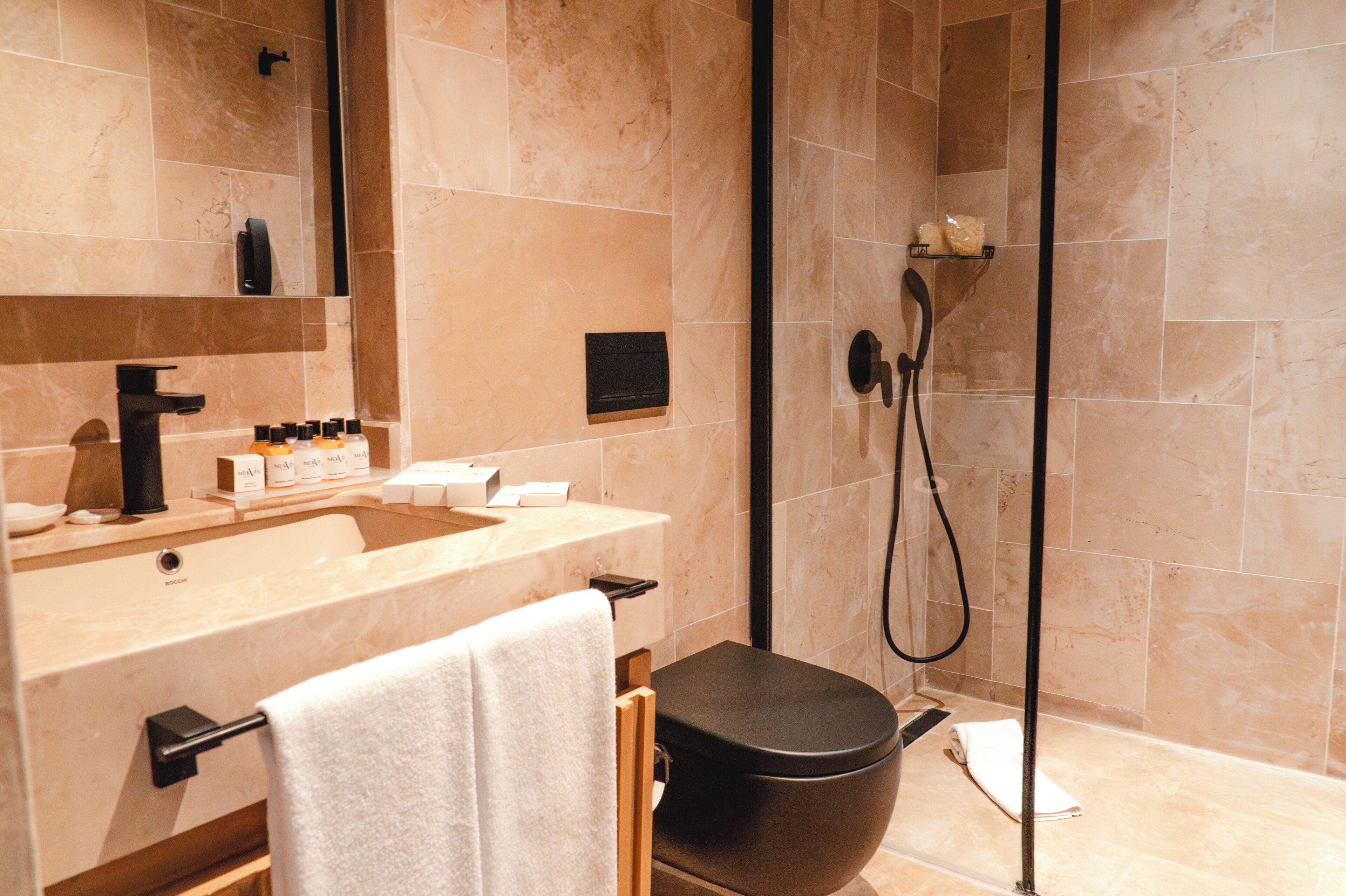 A modern bathroom with a beige marble sink, a black toilet, and a glass shower enclosure.