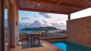 Zona de piscina al aire libre con mesa y sillas, un muro de piedra y vistas al mar y a las montañas.