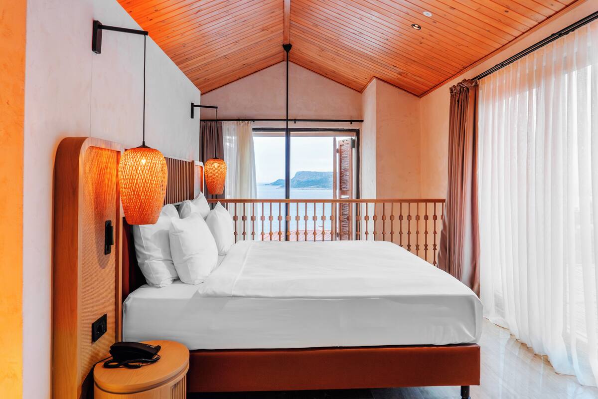 Habitación de hotel con una cama grande, techo de madera y vistas al mar.