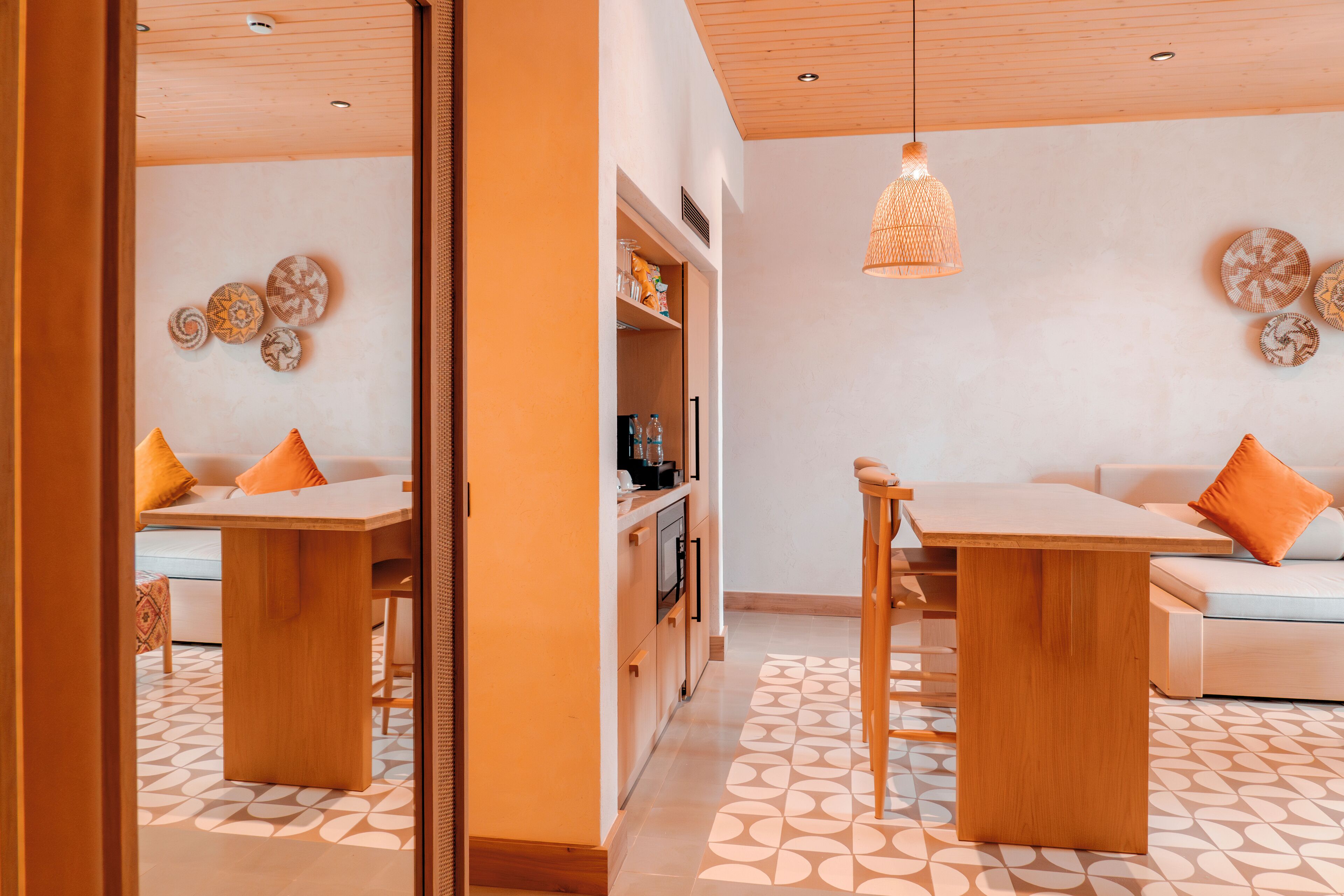 A modern living room with a sofa, two wooden tables, and a kitchen area with cabinets and appliances.