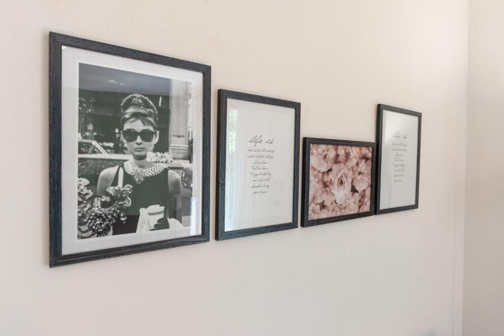 Eine Wand mit drei gerahmten Dekorationen: einem Schwarz-Weiß-Foto, einem gerahmten Text und einem Blumenmotiv.