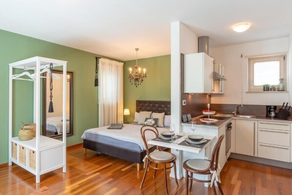 Una habitación de hotel compacta con una cama, una pequeña mesa de comedor, una kitchenette y un armario.