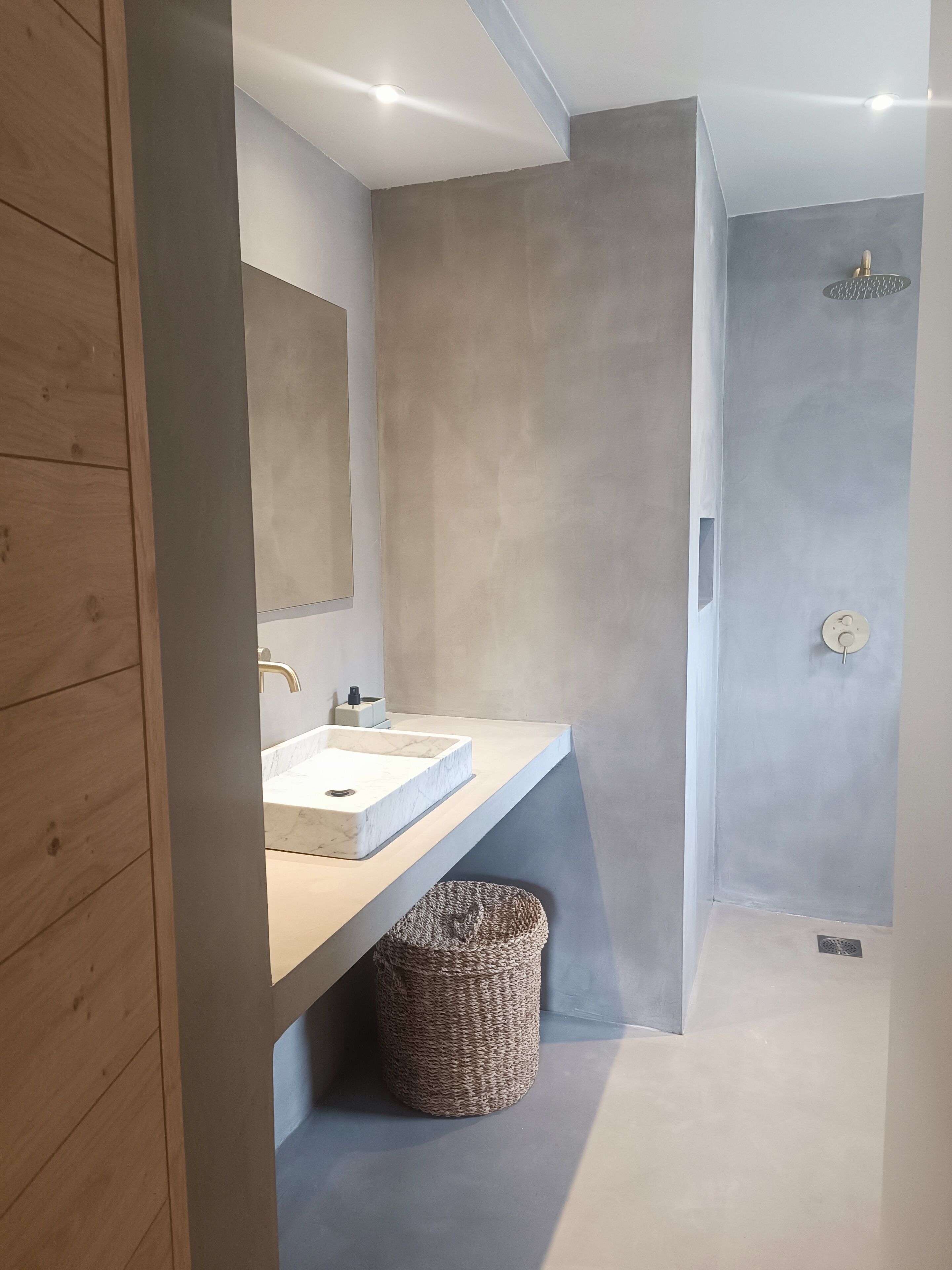 Un bagno moderno con un lavandino in marmo, uno specchio grande e una doccia con soffione a pioggia.