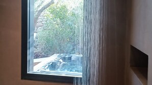 A shower with a window, water flowing from the showerhead, and a view of greenery outside.
