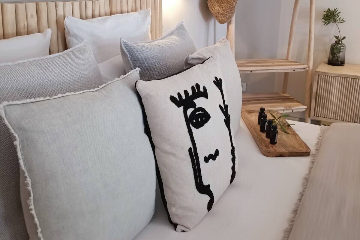 Une chambre à coucher bien aménagée, avec une tête de lit en bois, plusieurs oreillers, une table de chevet agrémentée d’une plante et un étendoir à linge suspendu.
