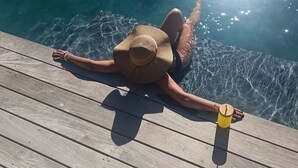 A person relaxing by a poolside with a sun hat and a yellow cup.