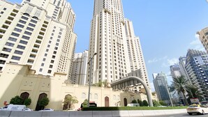 A tall, beige building with multiple floors and balconies, surrounded by other high-rise buildings. - WelHome - Waterfront Family-Size Apt With JBR Beach Access (Dubai)