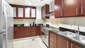 A modern kitchen with wooden cabinets, stainless steel appliances, and a tiled backsplash. - WelHome - Waterfront Family-Size Apt With JBR Beach Access (Dubai)
