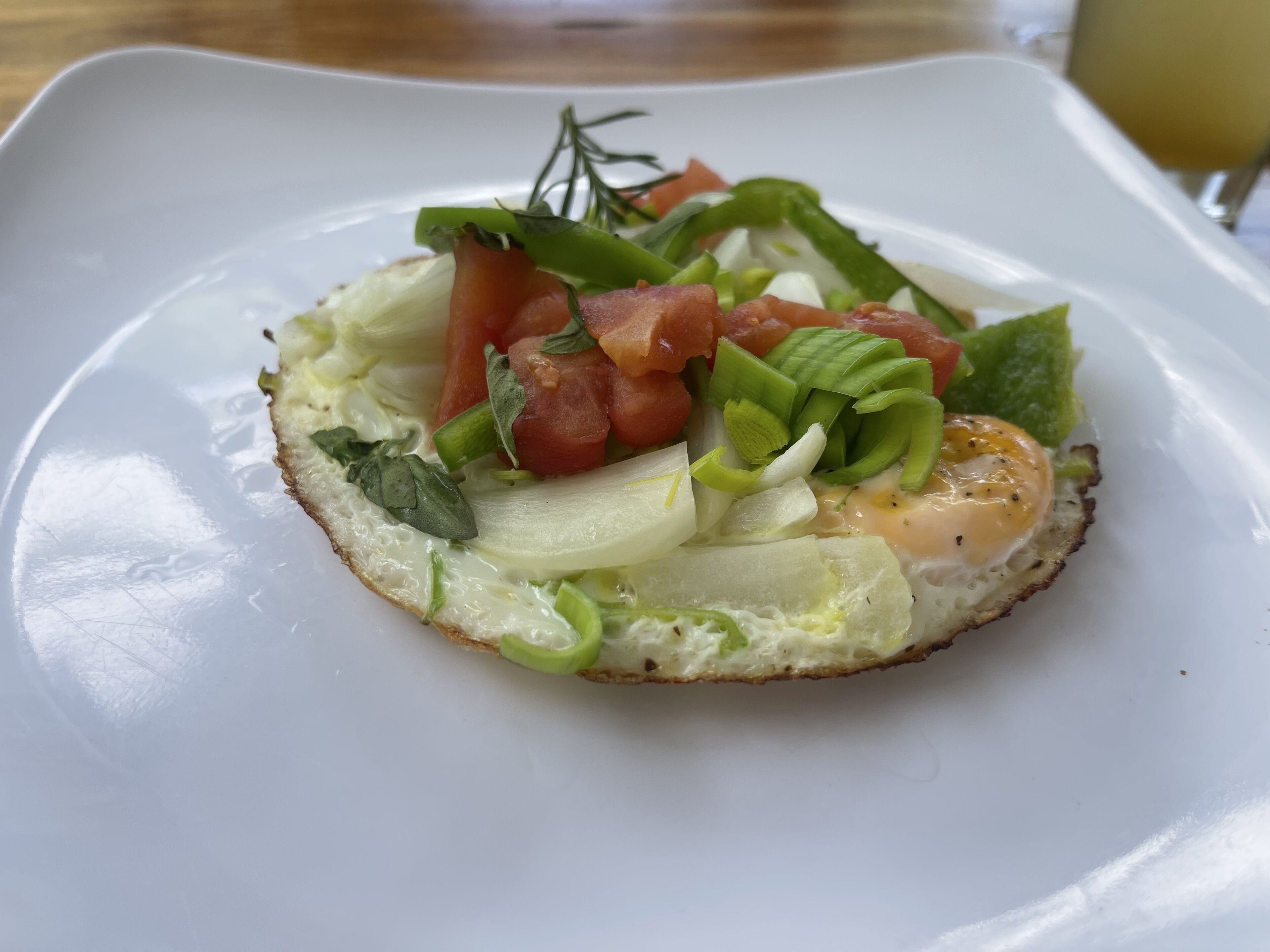 A white plate with a sandwich topped with lettuce, tomato, and a poached egg.