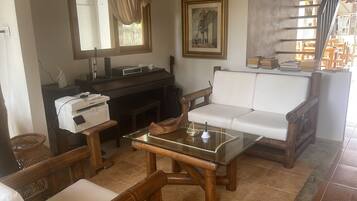 A living room with a white sofa, a glass coffee table, wooden chairs, a printer, a framed picture, and a bookshelf.
