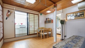 Una habitación japonesa tradicional con suelo de tatami, un panel corredizo shoji, una mesa de tatami con cuatro sillas, una cama de madera baja y un panel shoji colgante.