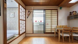 Una habitación tradicional japonesa con suelo de tatami, puertas correderas shoji, una pequeña cocina y una mesa de comedor con sillas.