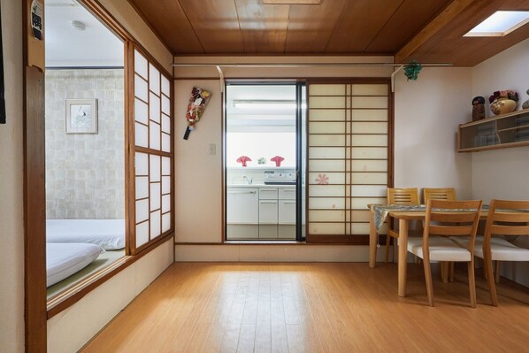 A traditional Japanese room with tatami flooring, a sliding shoji door, a small kitchen area, and a dining table with chairs.