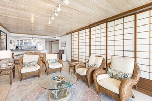 Un amplio salón con mobiliario de mimbre, una mesa de centro de vidrio y un tradicional mamparo japonés shoji.