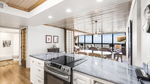 A modern kitchen with a large island, wooden flooring, and a view of the ocean through large windows. - Gulf Shores Condo 509 Beachfront Views & Coastal Gem (Port Aransas)