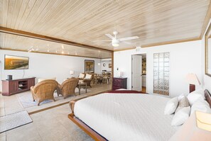 Un dormitorio amplio con una cama grande, techo de madera y un comedor con mobiliario de mimbre.