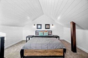 Une chambre avec un plafond en pente, un lit doté d’une tête de lit en bois, deux tables de chevet et une petite table de nuit.