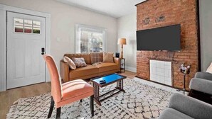 A living room with a brick accent wall, a flat-screen TV, a sofa, a coffee table, and a patterned rug.