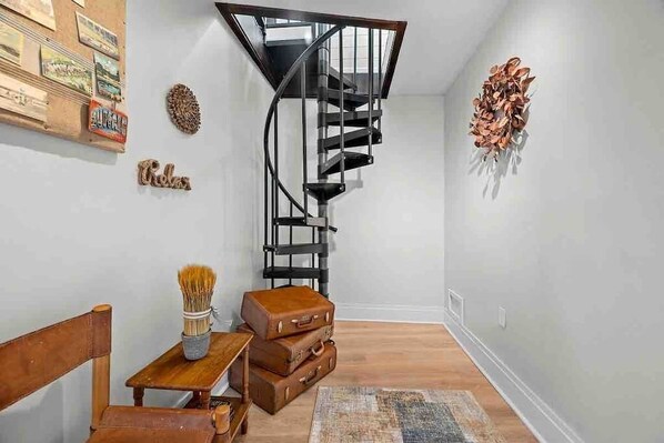 A staircase with a black metal railing, a wooden bench, a small table with a brush, and a wall with a decorative leaf arrangement.