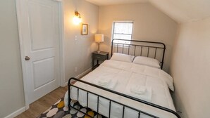 A bedroom with a bed, a nightstand, a lamp, a window, and a door. - Cozy & Comfy Cottage in the City - w/ parking! (Pittsburgh)