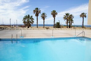 A swimming pool with clear blue water, surrounded by a tiled deck and palm trees.