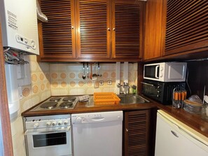 A compact kitchen with wooden cabinets, a microwave, a stove, and a dishwasher.