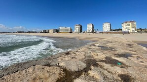 Una playa con un primer plano rocoso y edificios al fondo.