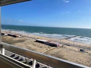 A beach view with a building, a parking lot, and a road.