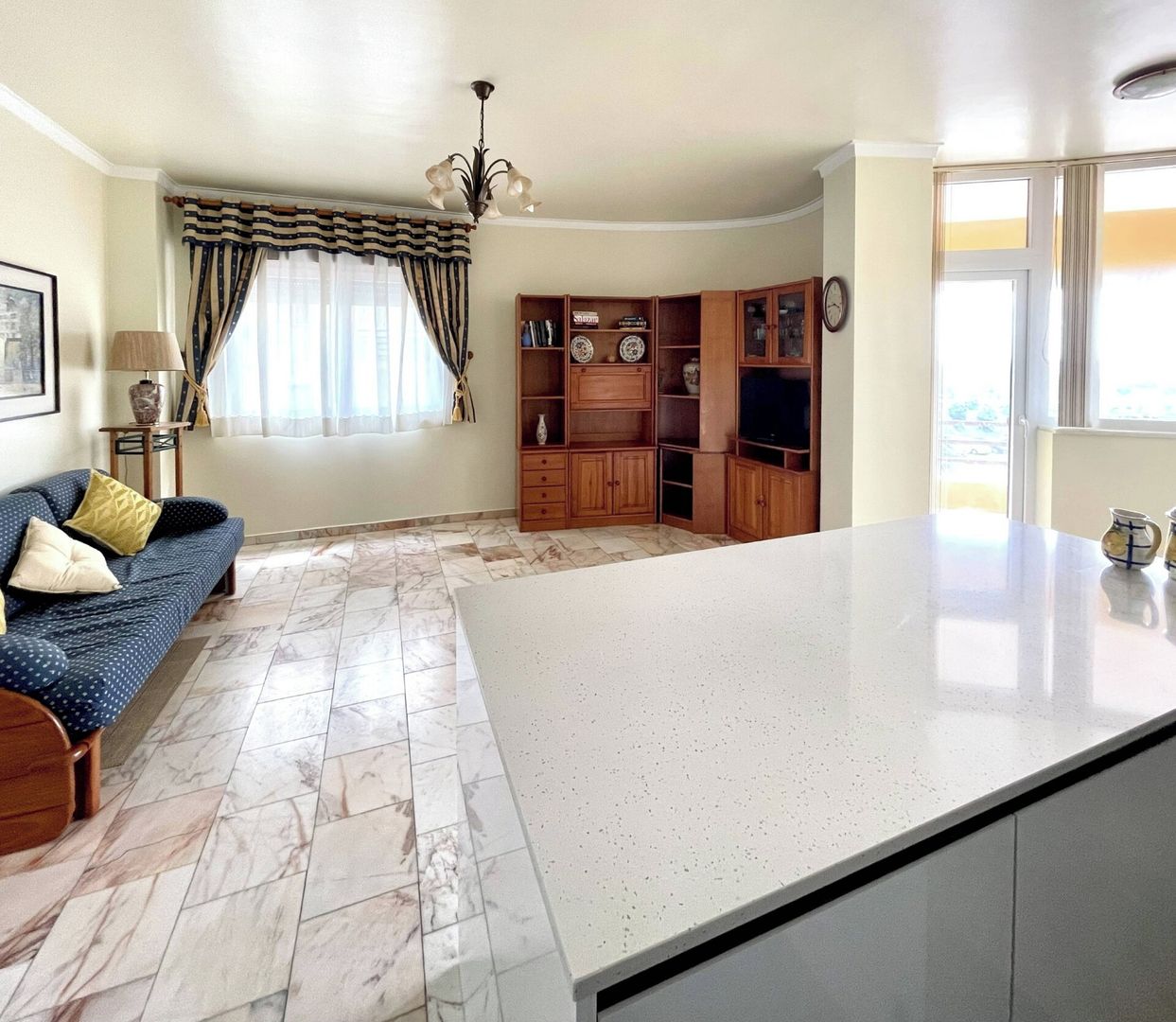 A living room with a sofa, a coffee table, and a kitchen area with cabinets and a television.