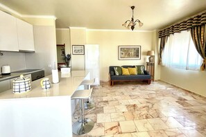 Un salon moderne avec un canapé, un coin repas et une cuisine en arrière-plan, ainsi qu’un lustre.