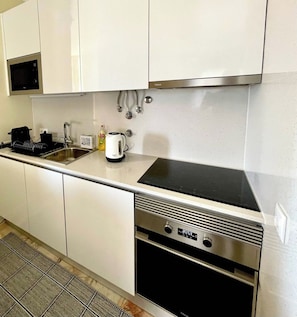 Une cuisine moderne avec des meubles blancs, un four en acier inoxydable et une plaque de cuisson noire.