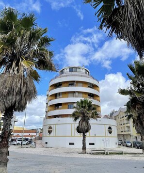 Un immeuble à plusieurs étages doté de balcons, entouré de palmiers et bordé de voitures garées.