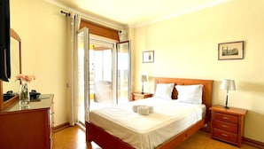 Habitación de hotel con cama, mesitas de noche, cómoda, espejo y puerta que da a un balcón.