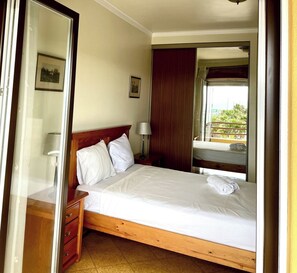 A hotel room with a single bed, a bedside table, a lamp, a wardrobe, and a window with a view of greenery.