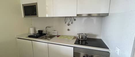 A compact kitchen with white cabinets, a stainless steel oven, a microwave, and a sink.