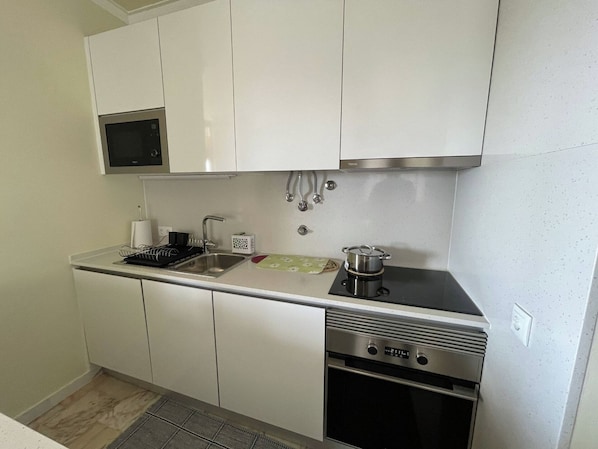 A compact kitchen with white cabinets, a stainless steel oven, a microwave, and a sink.