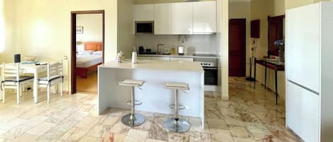 Una cocina moderna con una isla central, taburetes de bar y una zona de comedor con mesa y sillas.
