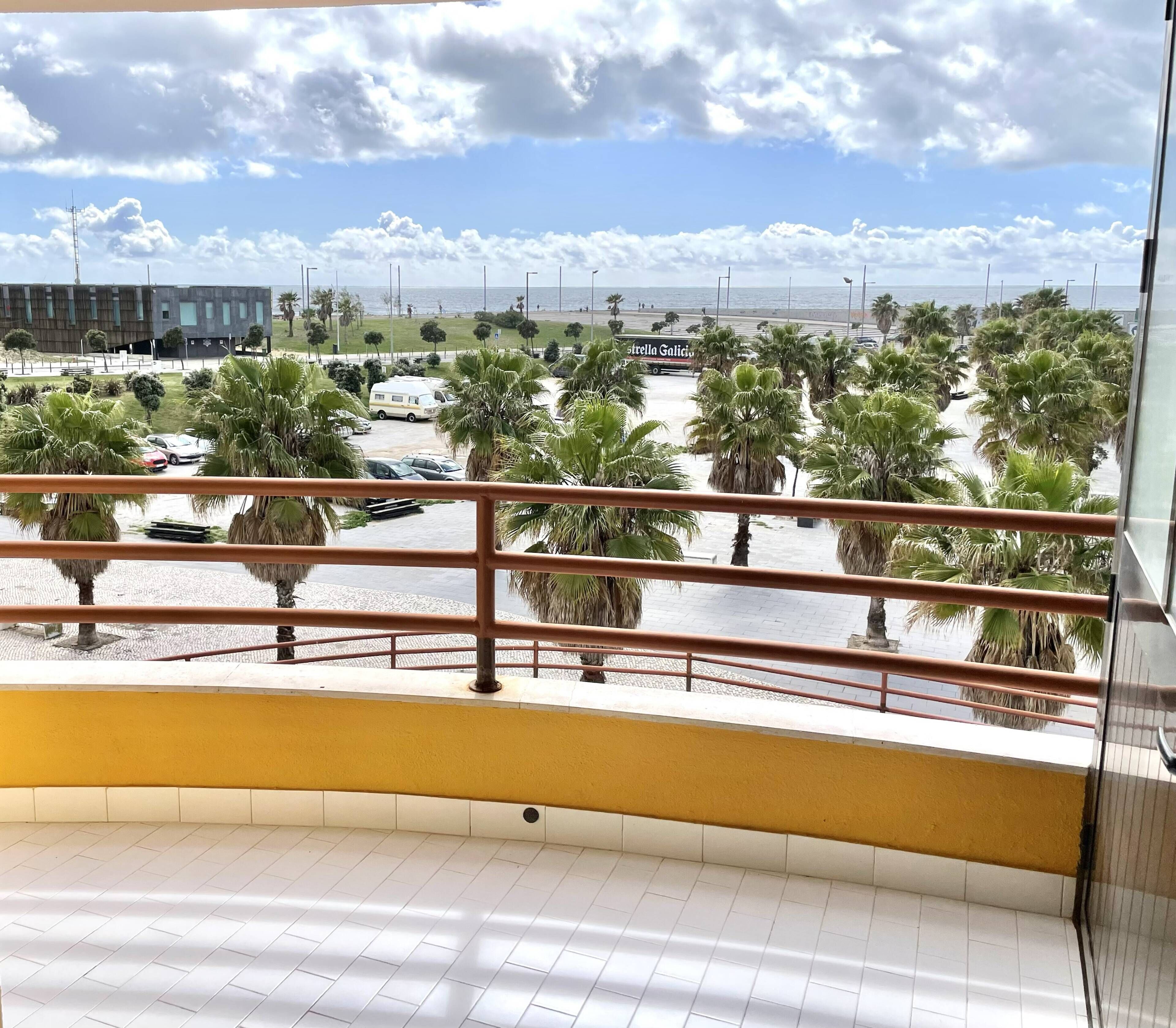 Un balcón con vista a un estacionamiento, palmeras y un edificio al fondo.