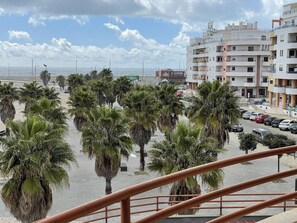 A coastal view with palm trees, a parking area, and a building with balconies. - Cozy apartment with a view of the sea (Almada)