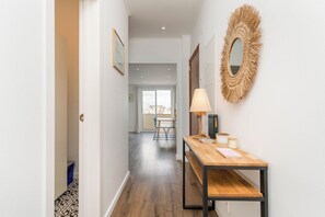 A hallway with a wooden table, a lamp, and a mirror on the wall. - Charming 2-bedroom apartment in Caparica (Almada)