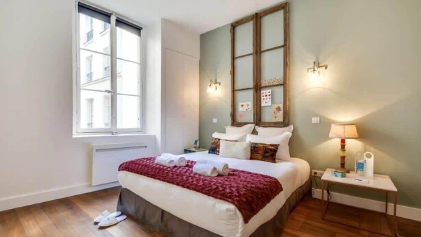 Una habitación de hotel con una cama grande, una ventana, una mesita de noche y una lámpara.