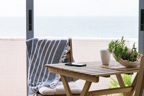 Ein Holztisch mit einem Smartphone, einer weißen Tasse und einem Blumentopf auf einem Balkon mit Blick aufs Meer.