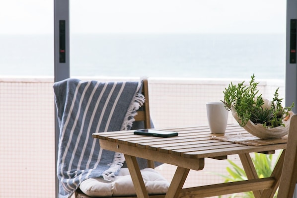 A wooden table with a smartphone, a white mug, and a potted plant on a balcony overlooking the sea. - Sunset Bliss - A Breathtaking Beachfront Apartment (Almada)