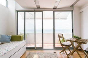 Un balcón con vista al mar, una mesa de madera con una planta y un sofá con cojines.