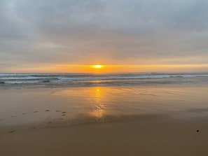 Uma praia com pôr do sol, ondas e pegadas.