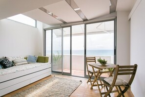 A modern living room with a sofa, a dining table, and a view of the sea through large glass doors. - Sunset Bliss - A Breathtaking Beachfront Apartment (Almada)
