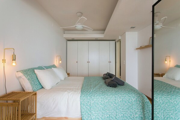 Un dormitorio con una cama, dos mesitas de noche, un armario, un ventilador de techo y un espejo.