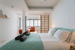 Quarto moderno com cama, sofá e vista para o mar através de grandes janelas.